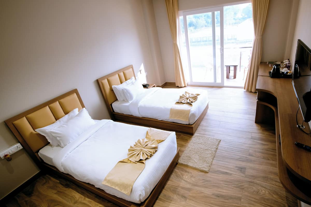 Une chambre d’hôtel avec deux lits, un plancher en bois, une télévision et une fenêtre avec des rideaux.