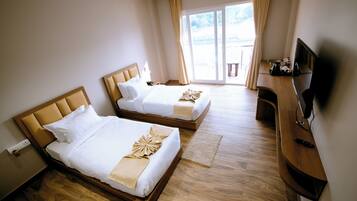 A hotel room with two beds, a wooden floor, a TV, and a window with curtains.