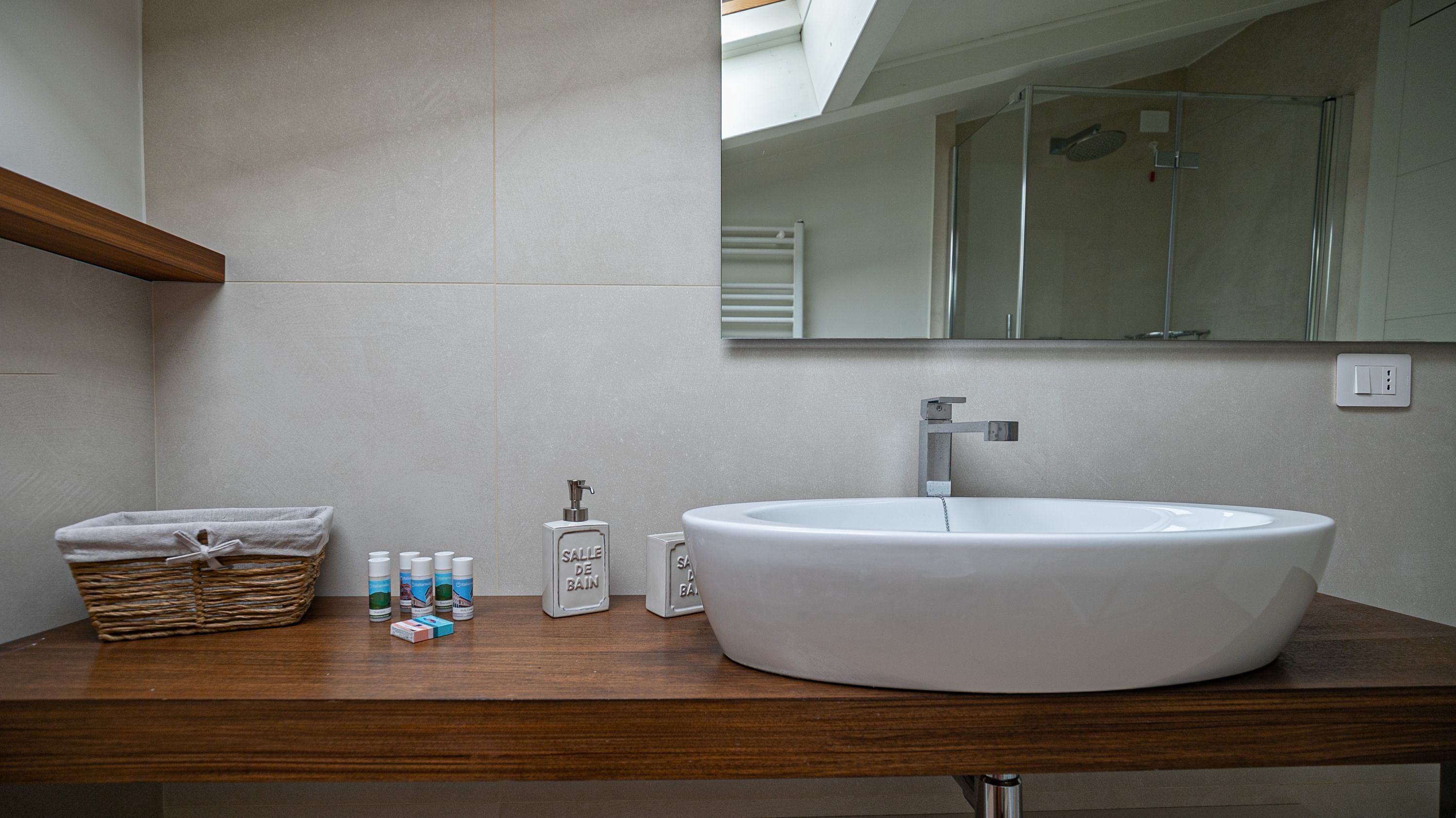 A bathroom with a large white sink, a wooden countertop, a mirror, and a shower area.