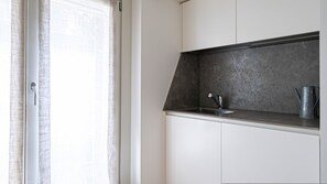 Een keuken met een donker aanrecht, een spoelbak en een metalen gieter.