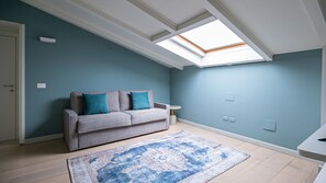 Een moderne woonkamer met een grijze bank, teal kussens, een kamerbreed tapijt en een dakraam.