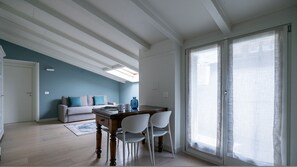 A dining area with a wooden table and chairs, a sofa, and a large window with sheer curtains. - Volta 40 in Monza With 2 Bedrooms and 2 Bathrooms (Monza)