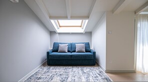 A room with a skylight, a blue sofa with pillows, and a patterned rug. - Volta 40 in Monza With 2 Bedrooms and 2 Bathrooms (Monza)