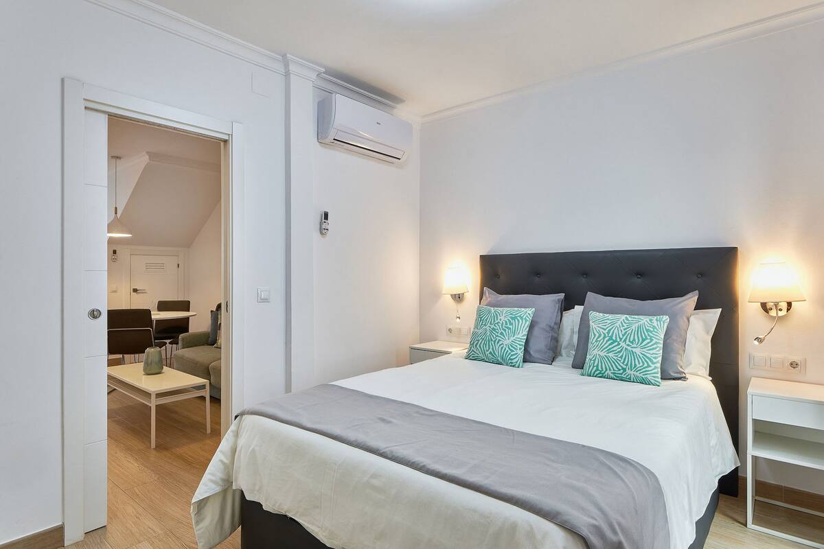Ein Schlafzimmer mit Bett, Nachttischen, einer Klimaanlage und Blick in einen anderen Raum.