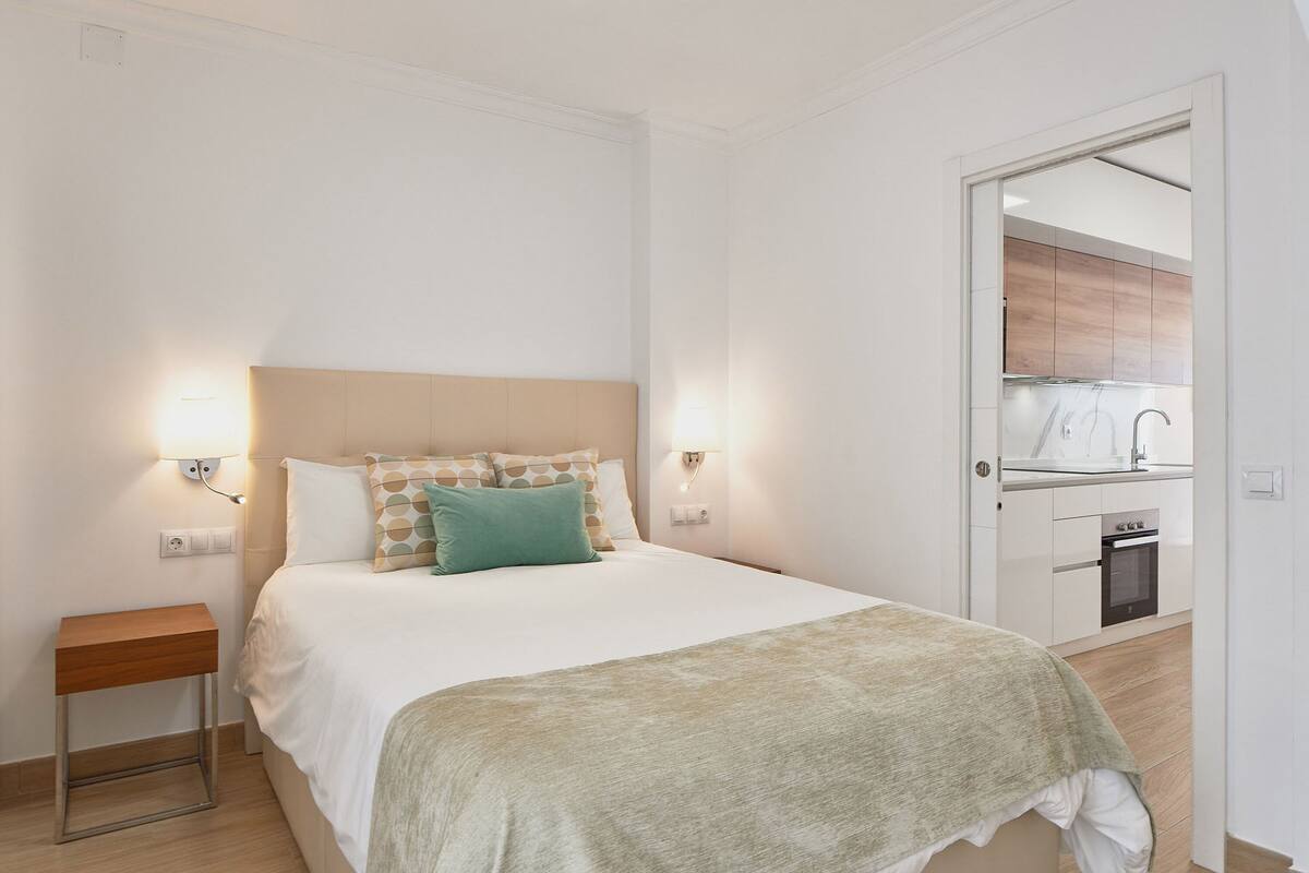 Ein Schlafzimmer mit Bett, Nachttischen und Blick in eine Küche.