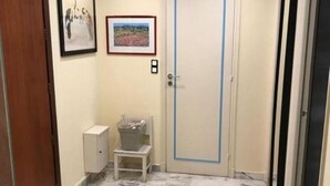 A hallway with a marble floor, a door with a blue frame, a small white cabinet, and two framed pictures on the wall.