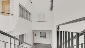 A narrow stairway with a metal railing, white walls, and a door at the top. - Alfa I (Machico)