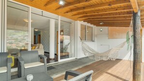 A spacious patio with wicker furniture, a hammock, and a view of a cityscape through large sliding glass doors. - Alfa I (Machico)