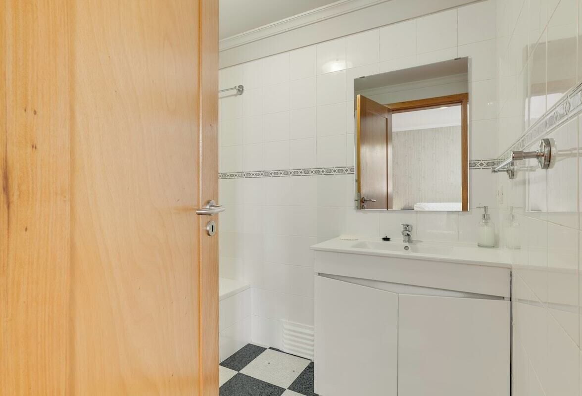 Un baño con lavamanos blanco, espejo y paredes con azulejos.