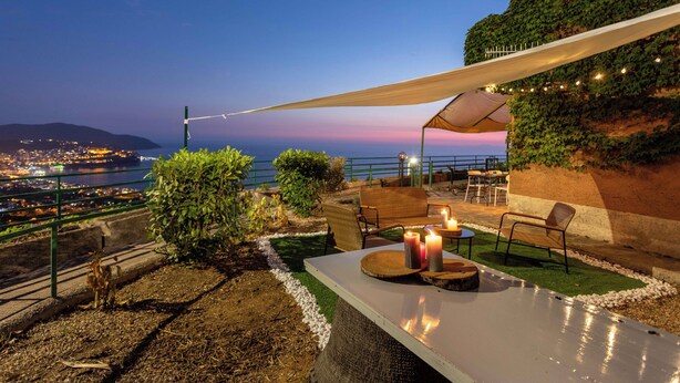 Een terras buiten met uitzicht op de stad in de schemering, met een tafel, kaarsen, stoelen en een zonnescherm.