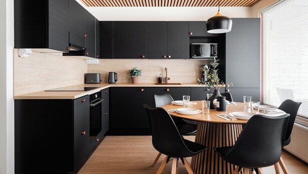 Een moderne keuken met zwarte kastjes, een houten aanrecht en een eethoek met zwarte stoelen en een houten tafel.