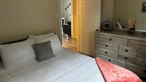 Une chambre à coucher comprenant un lit, une commode et une porte donnant sur une autre pièce.