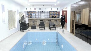 A swimming pool with a tiled floor, surrounded by seating areas and a reception desk. - G- throne Hotel and Suites (Port Harcourt)