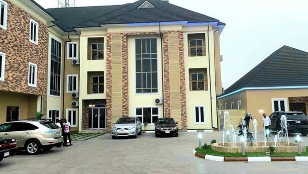 A multi-story building with a central entrance, a parking area with several cars, and a decorative fountain. - G- throne Hotel and Suites (Port Harcourt)
