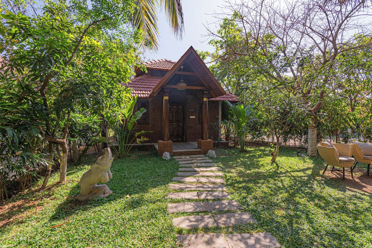 A rustic house with a stone pathway leading to the entrance, surrounded by lush greenery.