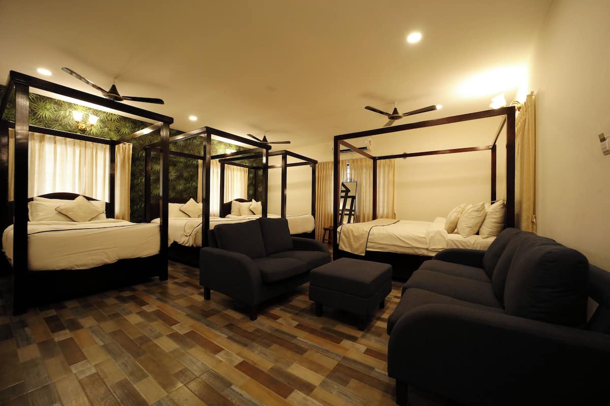 A room with four four-poster beds, dark sofas, and a wooden parquet floor.