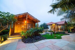 A wooden cabin-style building with a porch, surrounded by a landscaped garden with palm trees and a stone pathway. - Brown Town Resort & Spa (Hyderabad)