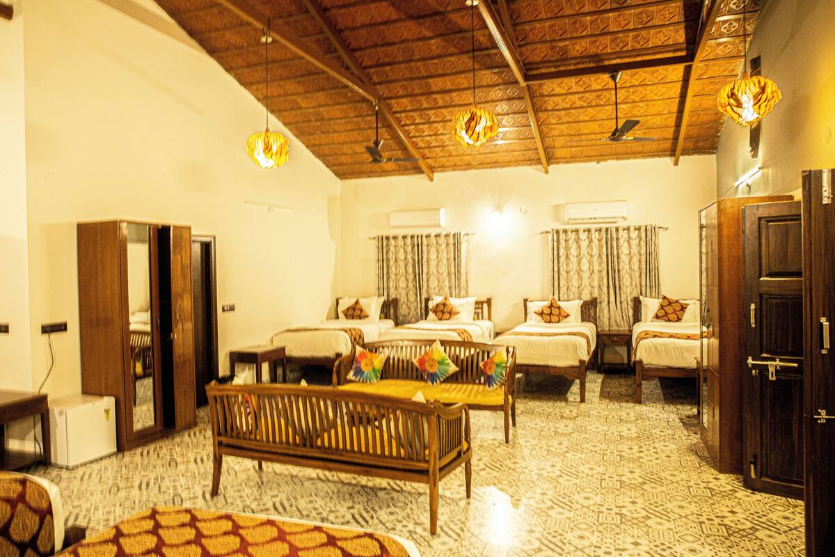 A hotel room with a wooden ceiling, two beds with patterned curtains, a wooden bench, and a small table.