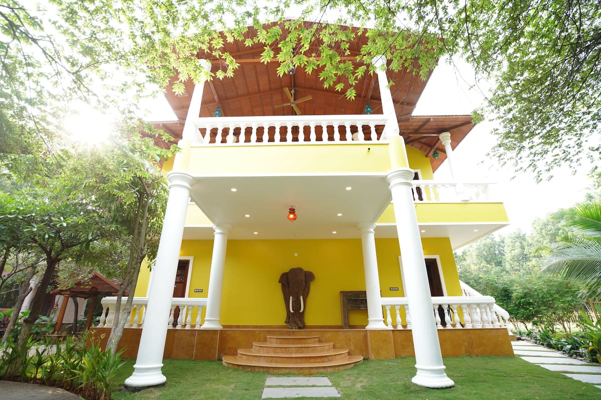 A yellow building with a large elephant sculpture at the entrance, white columns, and a covered balcony.