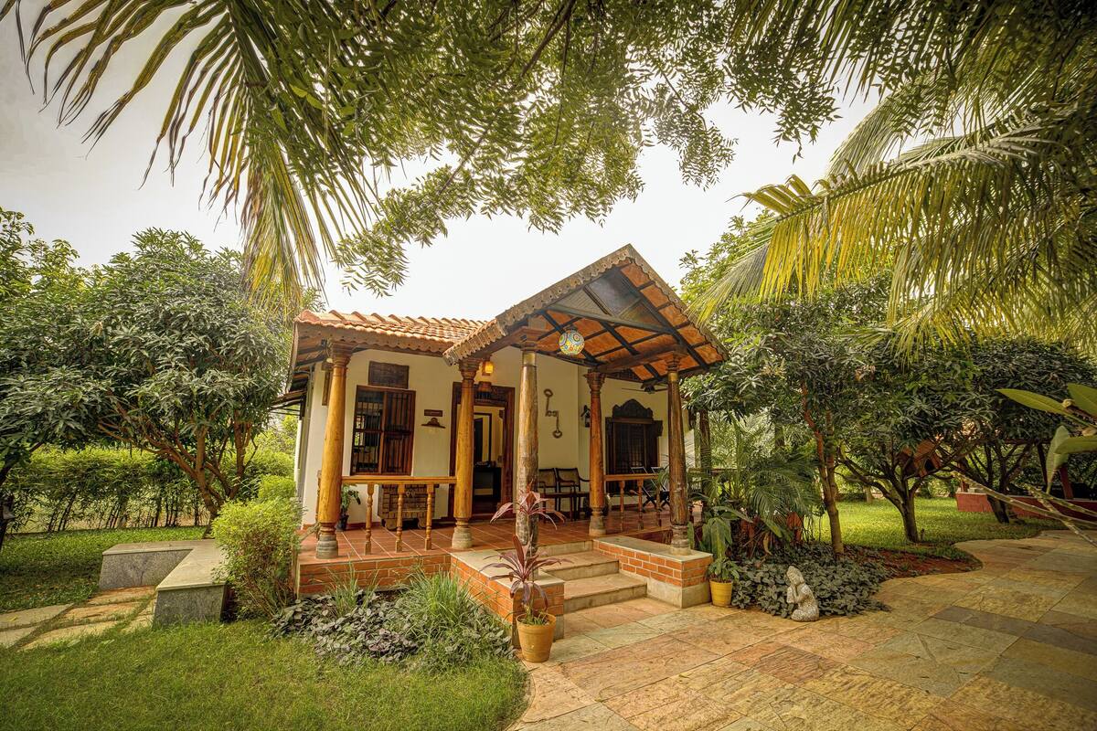 A traditional house with a tiled roof, a porch with wooden pillars, and a garden with various plants and a statue.