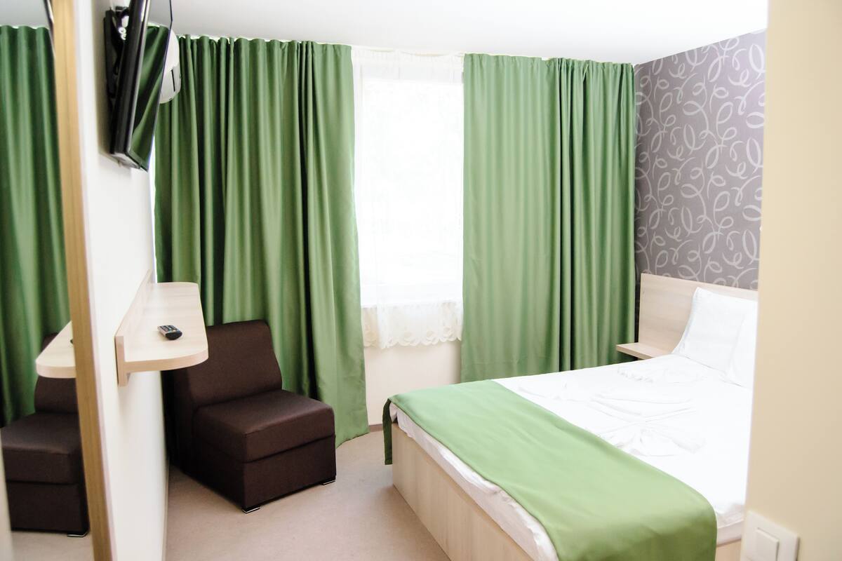 A hotel room with a bed, a chair, a desk, and a window with curtains.