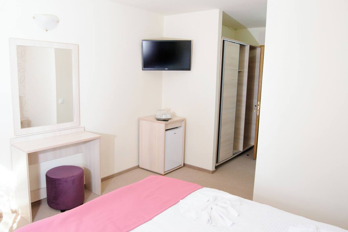 A bedroom with a bed, a desk, a small cabinet, a television, and a wardrobe.