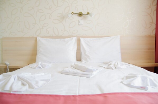 A neatly made bed with white linens, a bedside table with a lamp, and a wall with a leaf pattern. - Hotel Doina (Constanta)