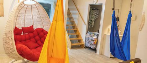 A spacious living area with a hanging chair, a hammock, and a staircase leading to a bedroom.