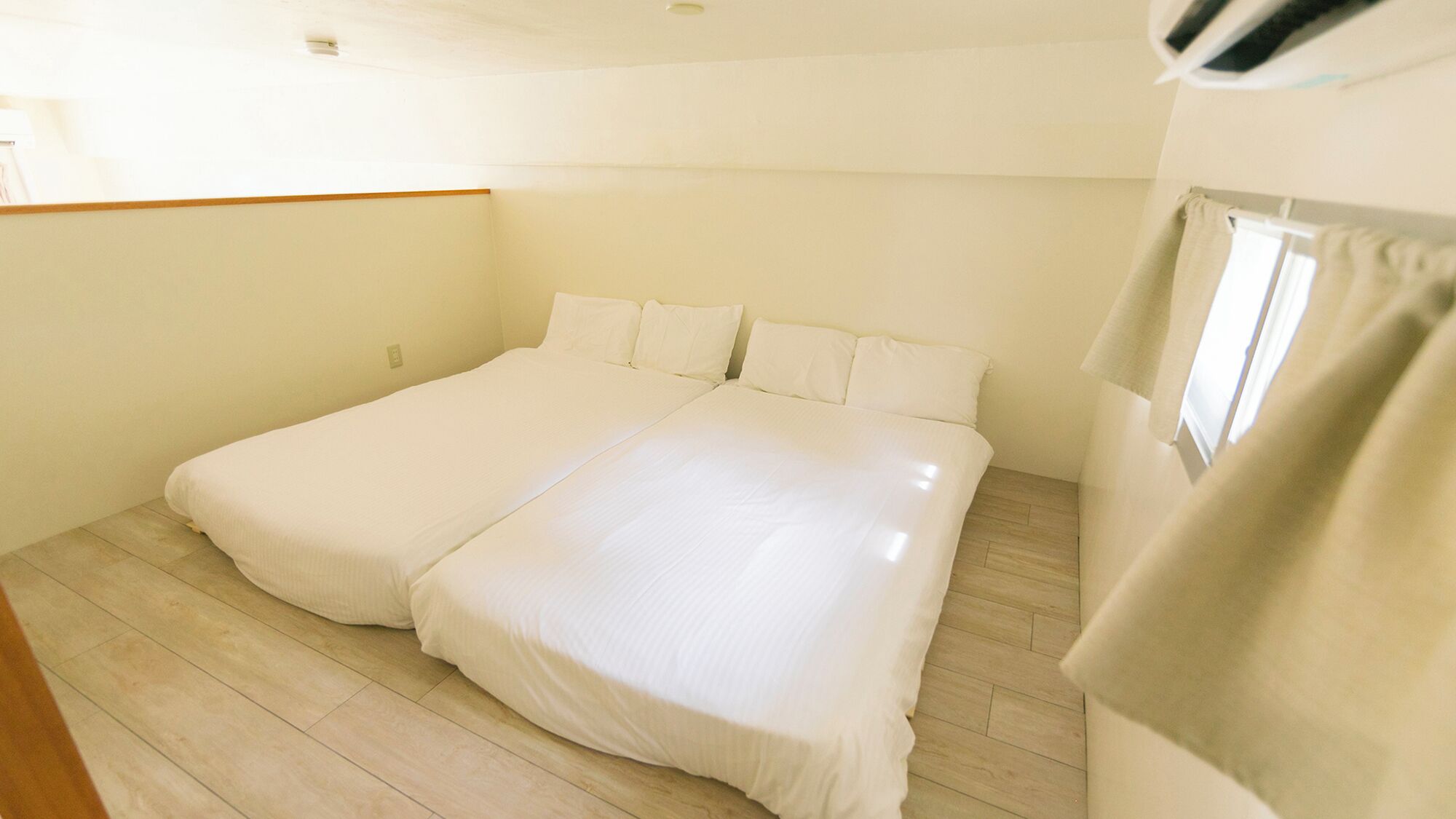 A bedroom with two beds, wooden flooring, and a window with curtains.