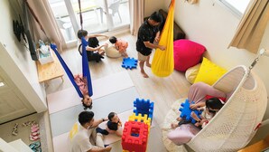 Un cuarto amplio con un ventanal grande, una silla colgante y una zona de juegos con bloques de construcción.