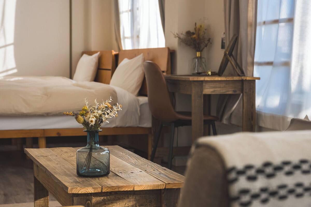A bedroom with a wooden bed, a wooden table with a vase of flowers, and a chair.