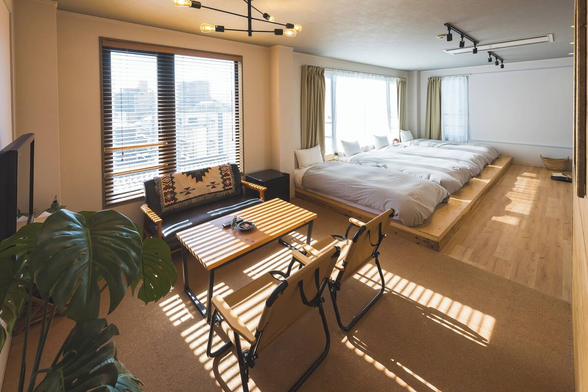 A hotel room with a bed, a desk, a chair, a plant, and a window with blinds.