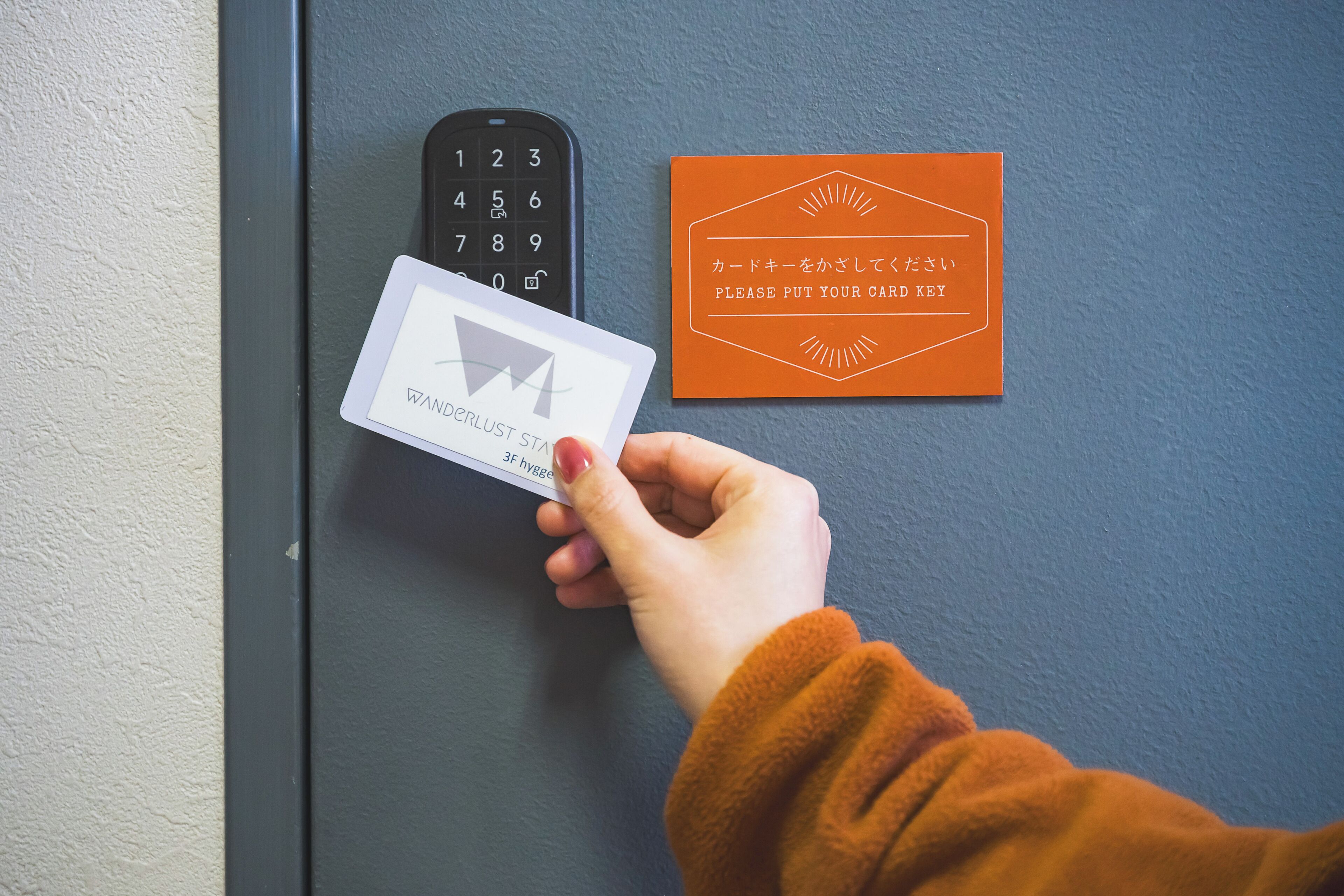 A hand holding a card near a keypad and a sign with Japanese text.