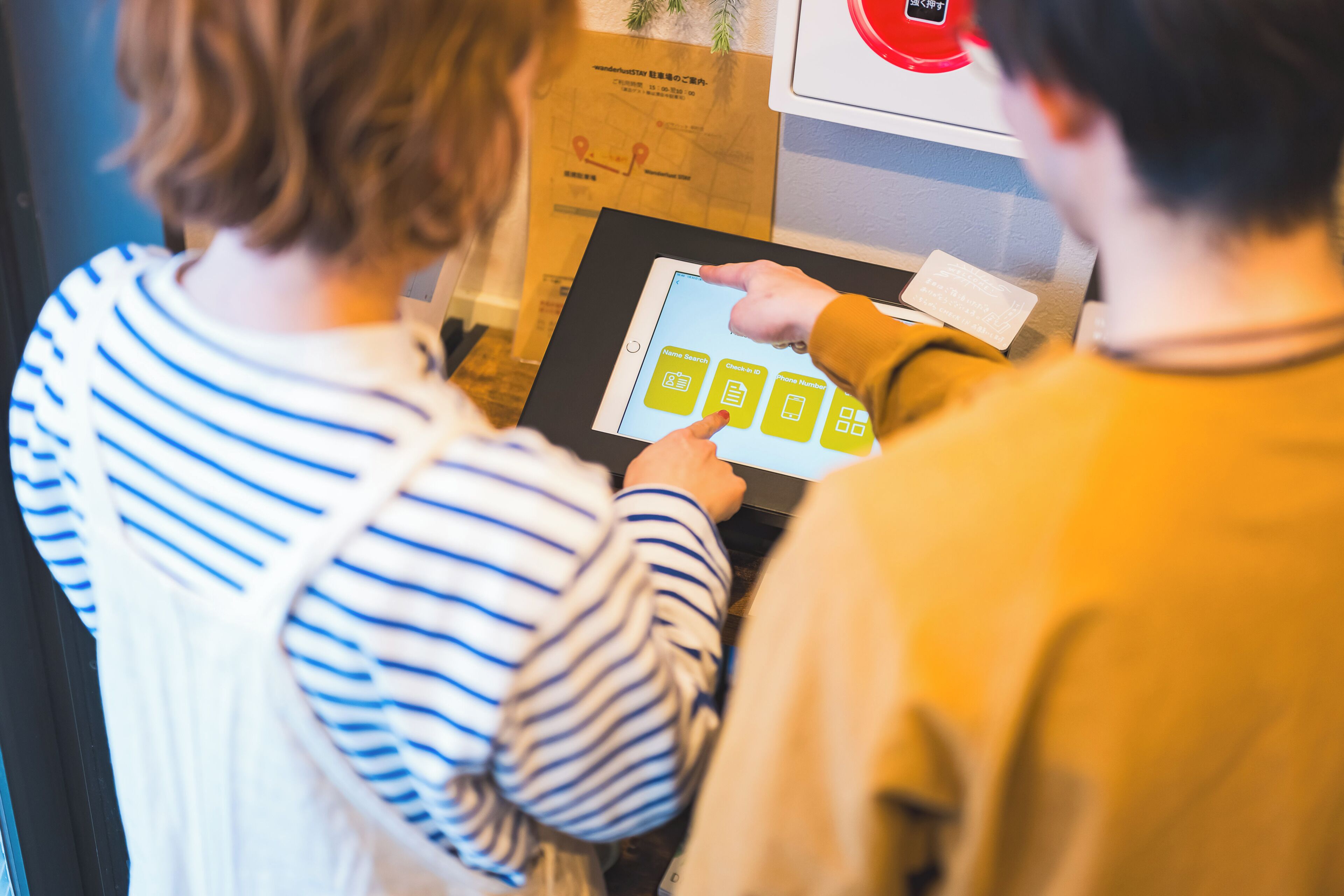 Twee personen gebruiken een digitale kiosk, mogelijk voor hotelincheck of informatie.
