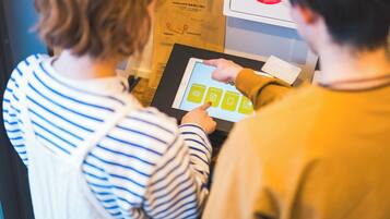 Twee personen gebruiken een digitale kiosk, mogelijk voor hotelincheck of informatie.