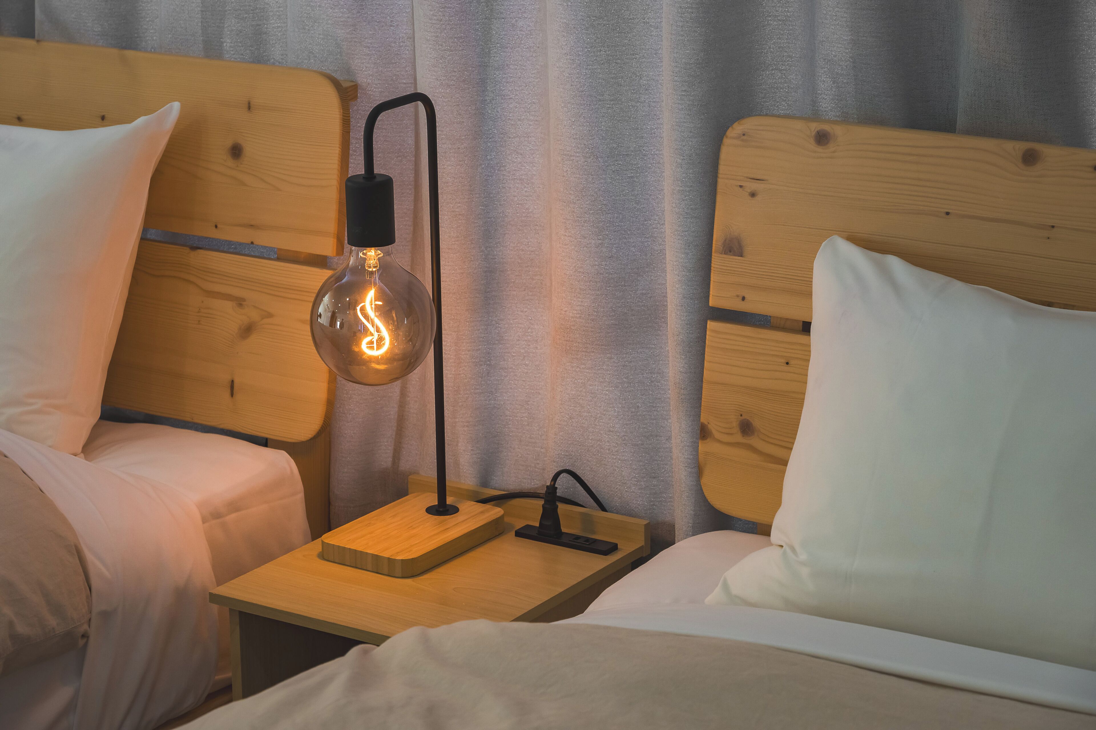 A hotel room with two wooden headboards, a bedside table with a lamp, and white bedding.