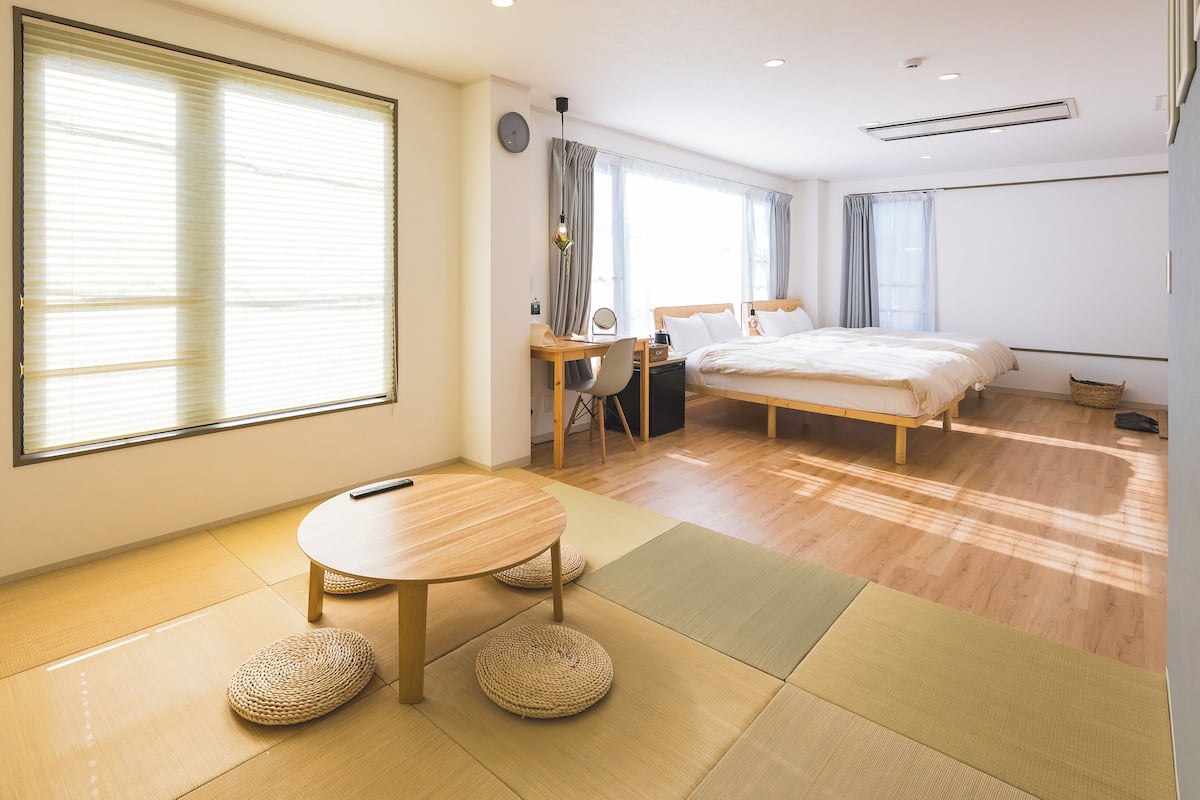 A modern bedroom with a bed, desk, chair, and a round table with tatami mats.