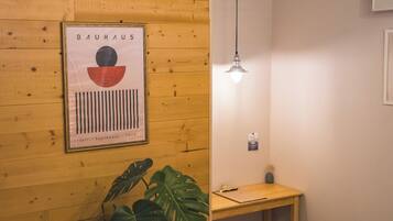 Una pared de madera con un cartel Bauhaus enmarcado, una planta en maceta, un escritorio y una lámpara colgante.
