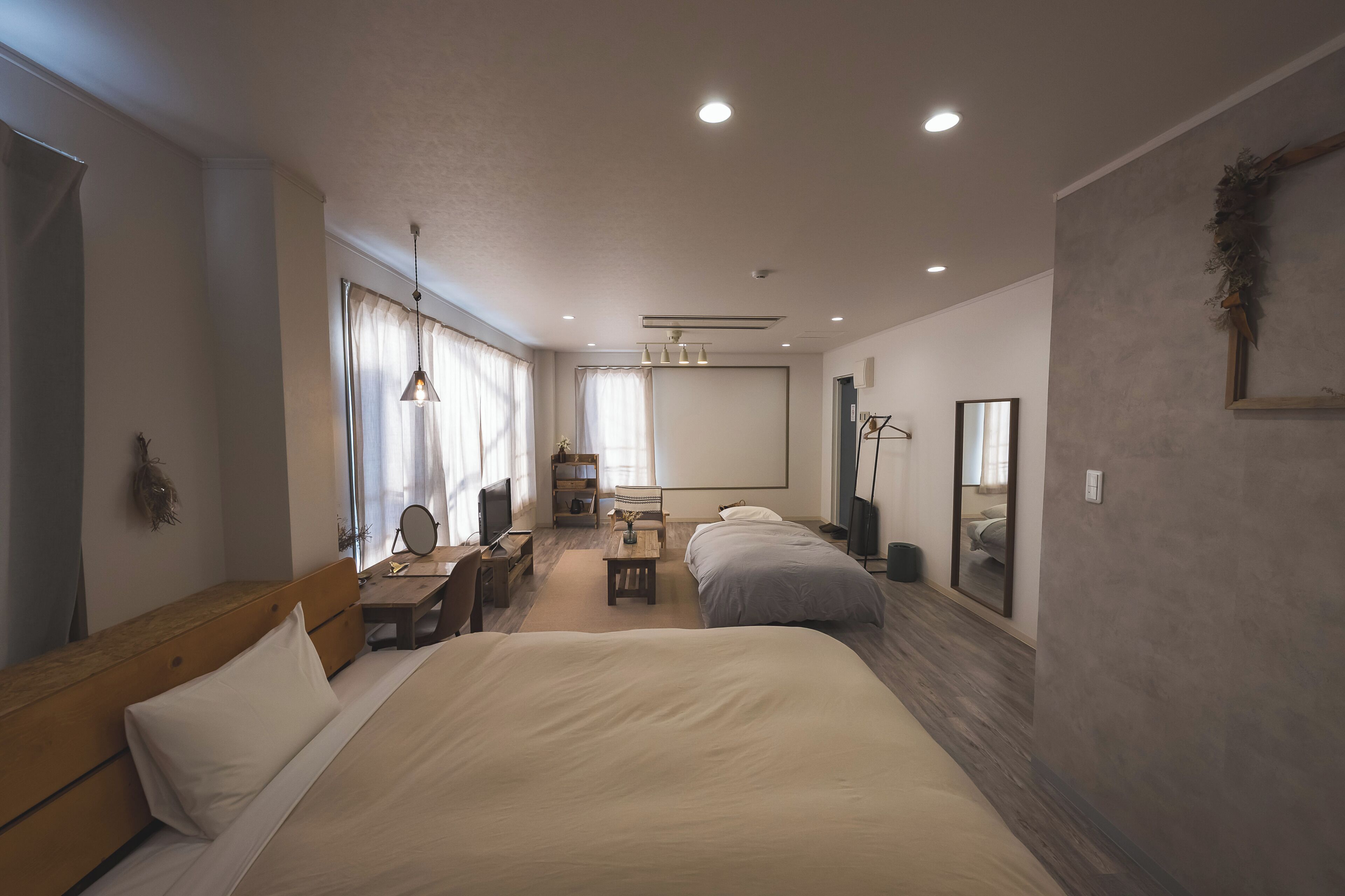 A hotel room with two beds, a desk, a chair, a mirror, and a television.
