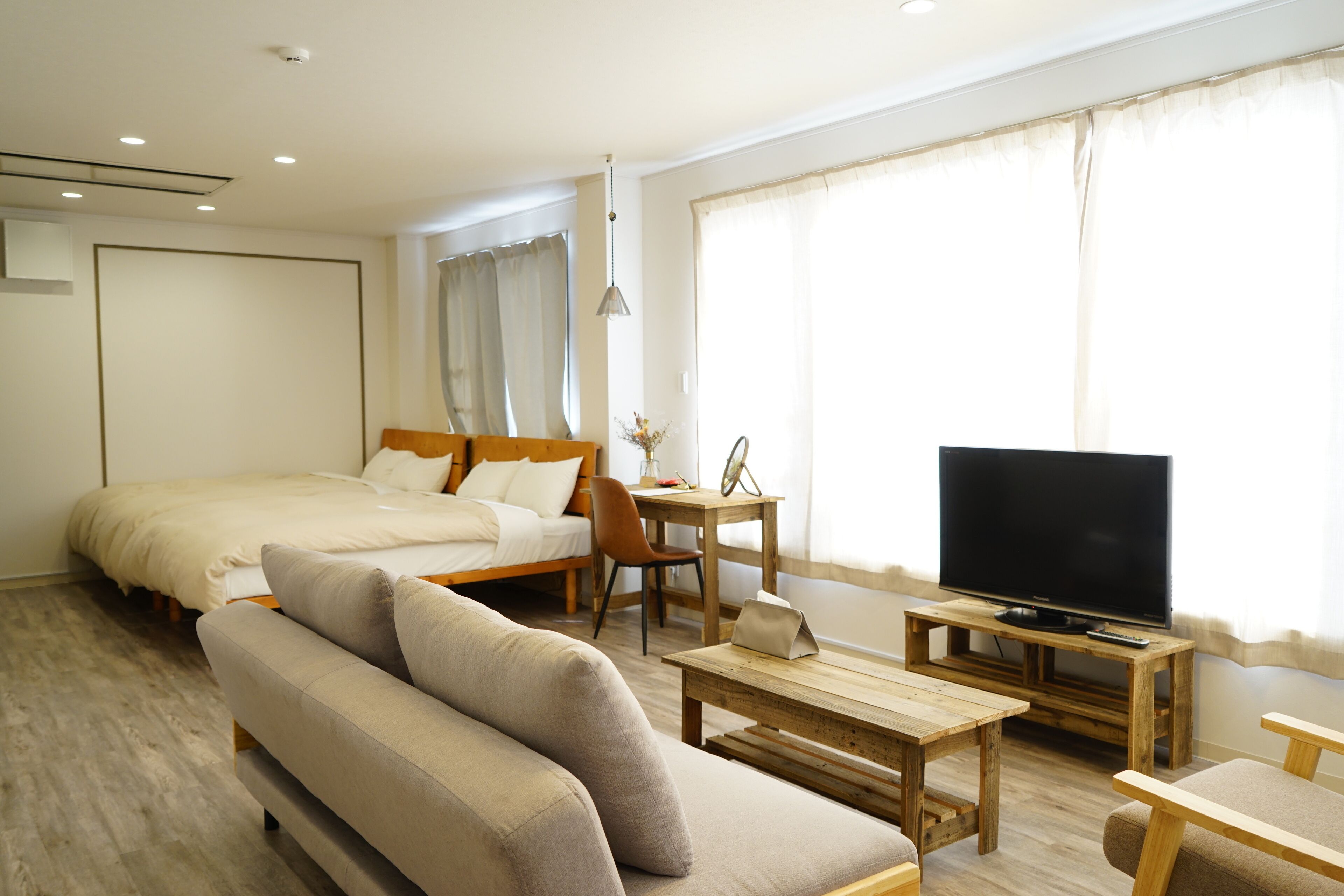 A modern hotel room with a large bed, a sofa, a TV, and a wooden coffee table.