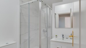 A modern bathroom with a glass-enclosed shower, a white sink with a gold faucet, and a mirror above the sink. - Funchal City Nest II (Funchal)