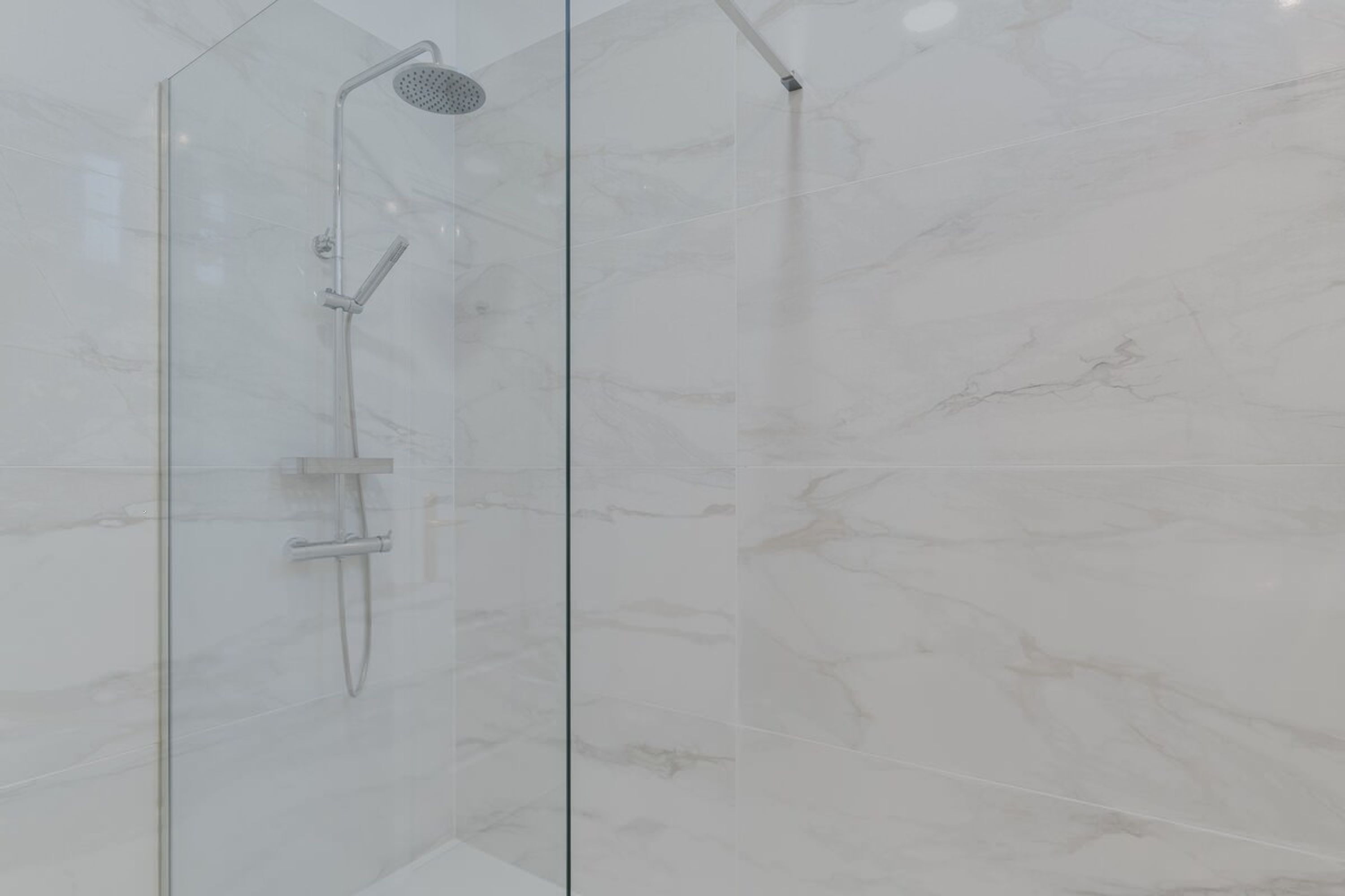 Eine Duschkabine mit Handbrause und am Wand montiertem Wasserhahn.