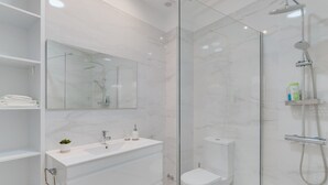 Ein modernes Badezimmer mit einer begehbaren Glasdusche, einem weißen Waschtisch mit Spiegel und einer Toilette.