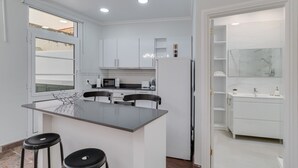 Eine moderne Küche mit weißen Schränken, einer zentralen Kochinsel mit Sitzgelegenheiten, einem Kühlschrank und einer Mikrowelle.