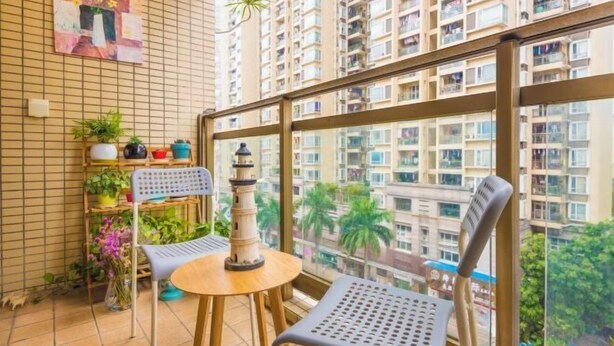 A balcony with a view of high-rise buildings, a small table, two chairs, and a shelf with plants and decorative items. - Muchun Apartment (Guangzhou)