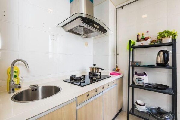 Una cocina moderna con un lavaplatos de acero inoxidable, una estufa a gas, un horno empotrado y una campana extractora negra. Se observa una repisa con diversos utensilios de cocina y una planta en maceta.