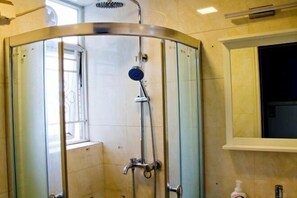 Una ducha con puerta de vidrio, una ventana y un perchero para toallas.