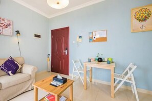 Una sala de estar con sofá, mesa de centro de madera, mesa de comedor con sillas, una puerta roja y obras de arte colgadas en la pared.