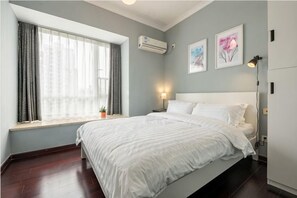 Un dormitorio con cama, ventana, aire acondicionado, una obra de arte y una mesita de noche.