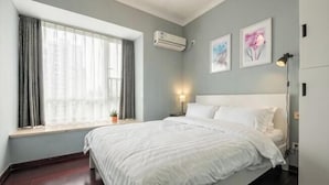 A bedroom with a bed, a window with curtains, an air conditioner, and wall-mounted artwork. - Muchun Apartment (Guangzhou)